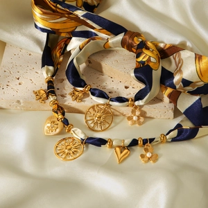 Detail of silk scarf necklace with golden sun, elephant, heart, and flower charms