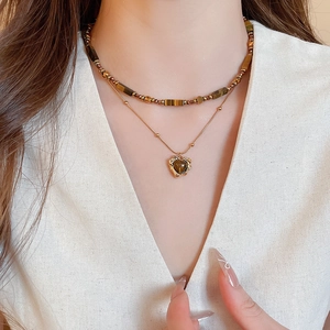 Close-up of double-layered heart pendant necklace with brown tiger eye beads on a model