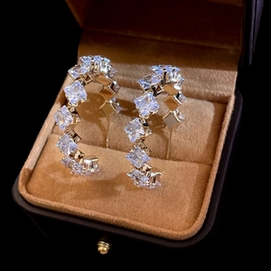 Macro view of C-shaped silver earrings with square-cut zircons in a brown velvet box
