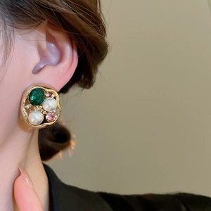 Close-up of vintage emerald and pearl stud earring on model with golden alloy details