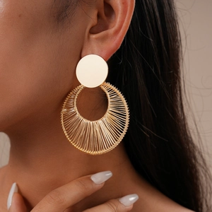Detail of model wearing gold hollow woven metal hoop earrings with a textured finish