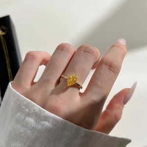 Close-up of elegant pear-cut yellow gemstone ring worn on finger in golden finish