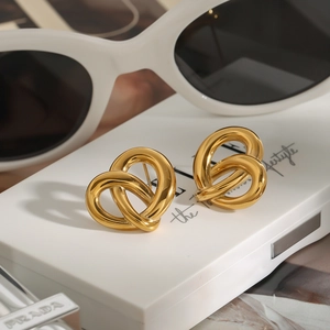 Goldene Herz-Knoten-Ohrringe aus poliertem Edelstahl auf einem minimalistischen weißen Ständer