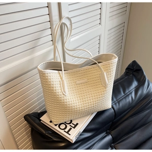 Detail shot of a cream woven tote bag with long straps beside a fashion book