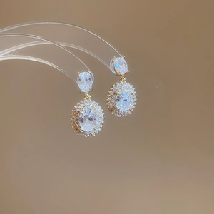 Detail of elegant gold oval zircon earrings hanging on a clear display stand with soft lighting