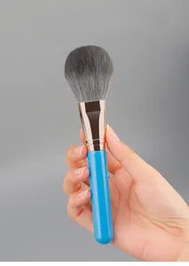 Detail of soft powder brush with royal blue handle and rose gold ferrule held by hand