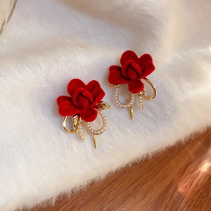 Dettaglio di orecchini a rosa in velluto rosso con fiocco dorato e perle eleganti