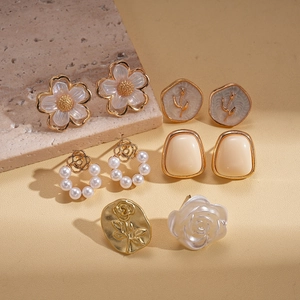 Macro shot of resin flower earrings and faux pearls on light stone background