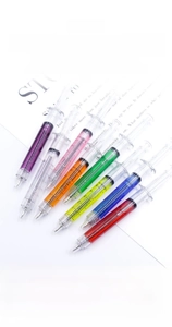 Detail showing 7 colorful syringe-shaped ballpoint pens with 0.5mm nibs on paper