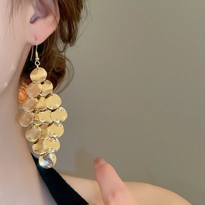 Close-up of golden multi-layer disc drop earrings worn on ear with metallic shine