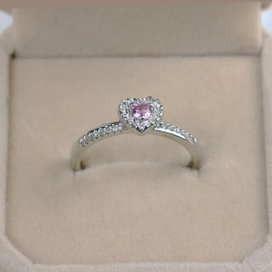 Detail of heart-shaped ring with pink center stone and white zircon accents in jewelry box
