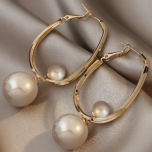 Detailed view of gold geometric hoop earrings with faux pearls on gray silk fabric