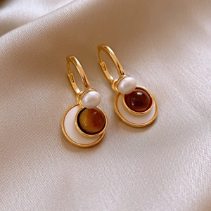 Close-up of gold hoop earrings with tiger eye stone and pearl on beige silk fabric