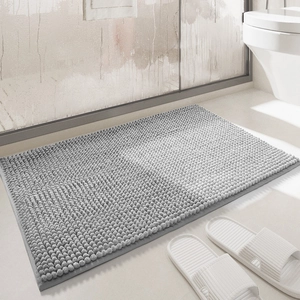Absorbent grey chenille bath mat on bathroom floor with white slippers as accessories