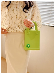 Limettengrüne EVA-Tasche mit Blumenanhängern, präsentiert von einem Model im sanften Licht
