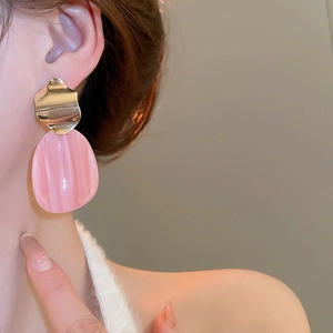 Close-up of elegant irregular pink oval resin earrings with wavy gold metal texture