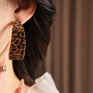 Close-up of model wearing a large C-shaped earring with brown leopard print and velvet texture