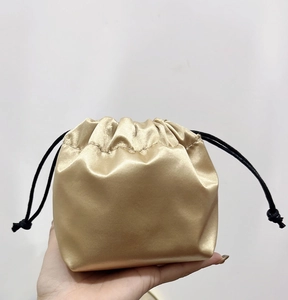 Detail of small gold satin drawstring gift bag held in hand for jewelry packaging