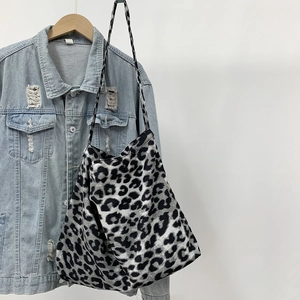 Detail of leopard print canvas tote bag hanging on a wooden hanger with denim jacket