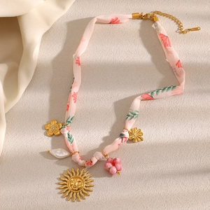 Detailed macro of 18K gold-plated sun and flower charms on pink fabric ribbon necklace