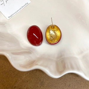 Macro view of red oval stud earrings with gold metal and hammer-textured back details