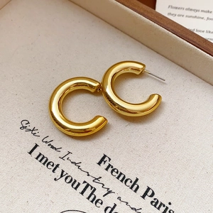 Vue détaillée de boucles d'oreilles créoles dorées en C sur une toile vintage texturée