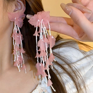 Detailed view of pink flower petal tassel earrings with white beads on a female model