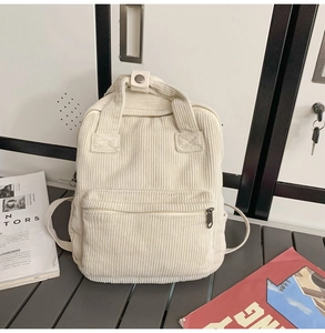 Detailansicht eines cremeweißen Cord-Rucksacks mit silbernen Beschlägen auf einem Tisch