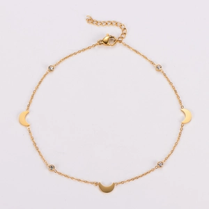 Macro shot of gold anklet with crescent moon charms and clear crystal pendants