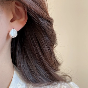 Detailed close-up of silver teardrop stud earrings with white cat eye stone on model
