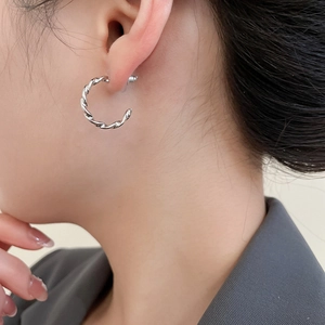 Nahaufnahme der gedrehten silbernen Creolen im minimalistischen Stil am Model