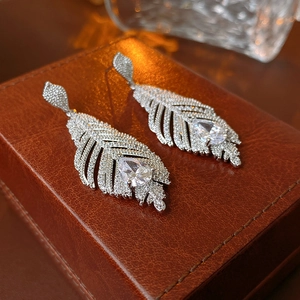Détail macro de boucles d'oreilles plume argentées avec zircons sur boîte en cuir