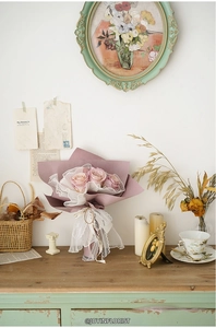 Detail of pink roses wrapped in white lace wave yarn and purple paper on a vintage cabinet
