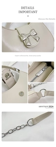 Detail of cream leather bag showing silver bow charm, metal zipper, and chain strap