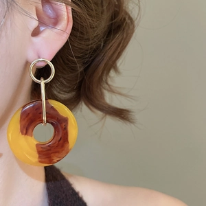 Close-up of a model wearing geometric resin hoop earrings with amber tortoise patterns