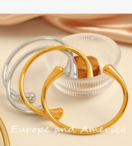 Dettaglio dei bracciali aperti a goccia color oro e argento su seta elegante