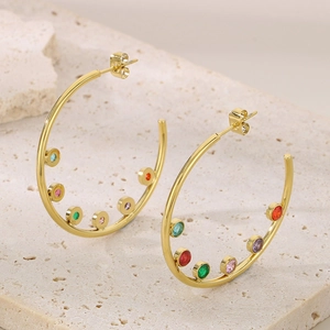 Detail of C-shaped gold earrings with colorful zircon stones on marble background