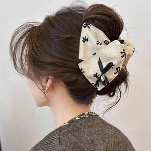 Detail view of cream linen bow hair clip with black prints and gold charm on model