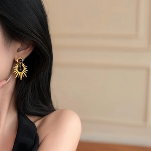 Detailed view of gold sunburst drop earring with brown tiger eye stone on model