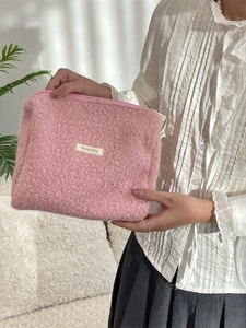 Roze fleece make-uptas met pluche textuur en minimalistisch label in de hand