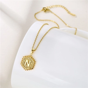 Detailed view of golden hexagonal letter N pendant with textured finish on a white surface