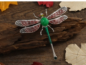 Detail of vintage dragonfly brooch with green gems and reddish enamel on wood texture