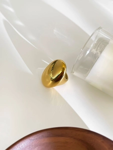 Macro shot of a bold oval golden stainless steel ring on a white reflective surface