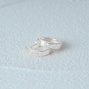 Detail shot of S925 sterling silver huggie earrings featuring three inset zircon stones