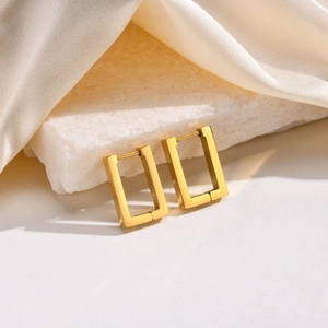 Close-up of minimalist gold-tone octagonal hoop earrings resting on white silk fabric