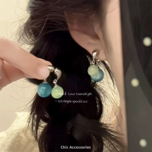 Détail de boucles d'oreilles en perles de verre bleu et vert sur mannequin avec fond brun