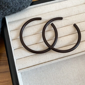 Macro view of large dark brown acrylic hoop earrings with a glossy finish on beige tray