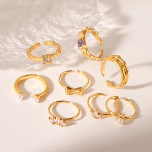 Set of 7 gold bow pearl and zircon adjustable stainless steel rings on white surface