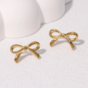 Minimalist golden bow stud earrings in stainless steel on white decorative block