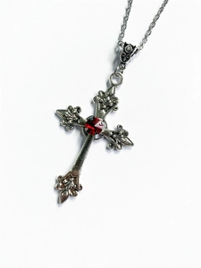Detailed view of silver cross necklace with ornate textures and a center red gemstone